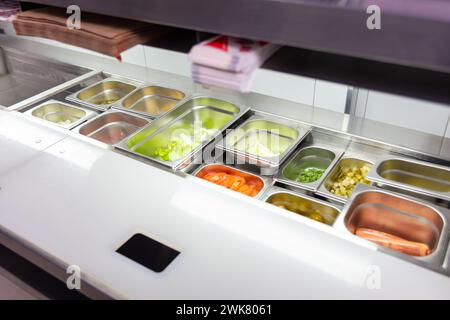 Ein Tisch mit Behältern mit Zutaten zum Kochen von Fast Food in der Küche eines Cafés, einer Pizzeria oder eines Restaurants. Stockfoto