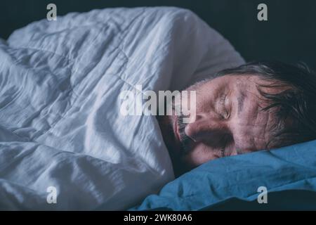 Müder schlafender Erwachsener, männlich in einem Bett auf blauem Kissen, selektiver Fokus Stockfoto