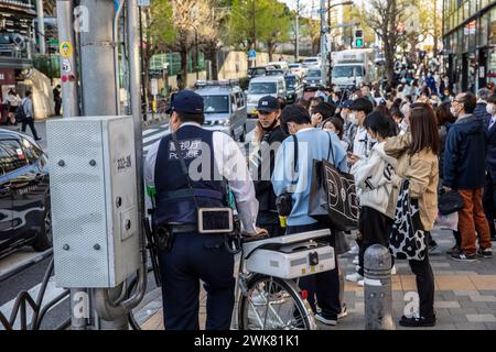 Harajuku Tokyo, japanischer Polizist zu Fuß mit seinem Fahrrad, wartet auf die Überquerung der Straße mit Menschenmassen der Einheimischen, Tokio Street Scene, Japan, 2023 Stockfoto