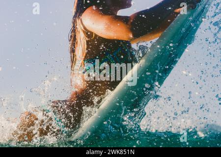 Eine Surferin in Einem Bikini geht über Eine Breaking Wave auf ihrem Surfbrett Stockfoto