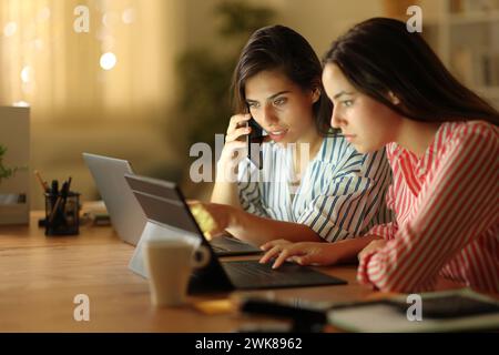 Zwei freiberufliche Mitarbeiter überprüfen den Laptop und rufen nachts zu Hause an Stockfoto