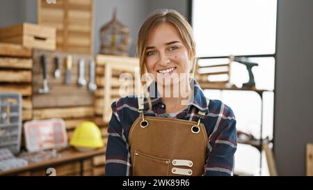 Ein lächelnder junger blonder Zimmermann, ein Porträt des Vertrauens, der stolz in ihrer Tischlerei steht Stockfoto