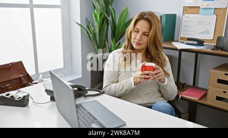 Hispanische Frau, die sich mit Kaffee im modernen Büro entspannt Stockfoto