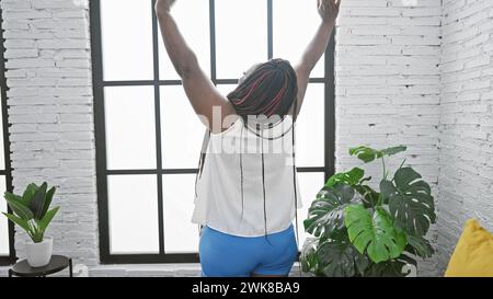 Im Komfort von zu Hause, schöne afroamerikanische Frau, die Arme streckt und die morgens Entspannung im Schlafzimmer genießt, während sie aufwacht, mit Blick von Stockfoto