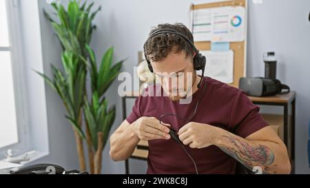 Ein junger hispanischer Mann mit Bart und Tätowierung passt sein Headset in einem modernen Büro an. Stockfoto