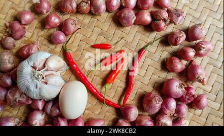 Foto von Gewürzen in Form von Schalotten, Knoblauch, Chilis und Eiern, die in einem gewebten Bambus angeordnet sind Stockfoto