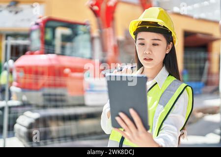 Junge chinesische Architektin, die auf der Straße über das Touchpad auf dem Smartphone spricht Stockfoto