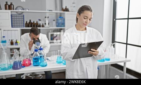 Wissenschaftler arbeiten im Labor zusammen, konzentrieren sich ernsthaft auf ihre Forschung, schreiben auf Zwischenablage, verwenden Mikroskop Stockfoto