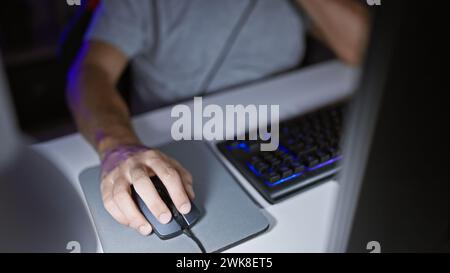 Ein Mann benutzt nachts eine Maus in einem schwach beleuchteten Spielzimmer, um auf einer hinterleuchteten Tastatur zu tippen, was auf Technologie und Freizeit hindeutet. Stockfoto
