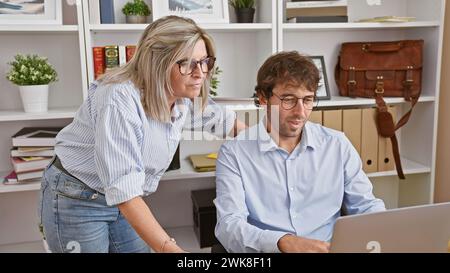 Zwei hart arbeitende Büroangestellte, ein Mann und eine Frau, die gemeinsam intensiv an einem Laptop arbeiten und das Bild eines unaufhaltsamen Teams projizieren. Stockfoto