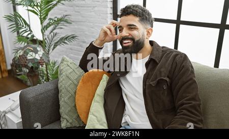 Ein fröhlicher Mann mit Bart sitzt lässig in einem modernen Wohnzimmer und strahlt Stil und Komfort aus. Stockfoto