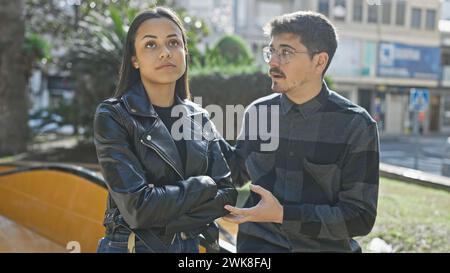 Ein Paar, das ernsthaft auf einer sonnigen Stadtstraße diskutiert und die Sorge zwischen einem Mann und einer Frau in lässiger Kleidung aufnimmt. Stockfoto