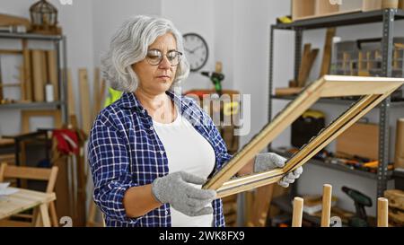 Eine reife Frau untersucht einen Holzrahmen in einer gut ausgestatteten Tischlerei Stockfoto
