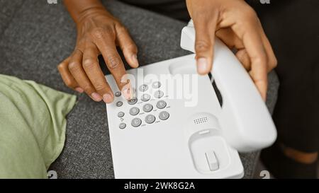 Nahaufnahme einer afrikanerin, die drinnen ein weißes Festnetztelefon wählt. Stockfoto