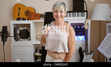 Lächelnde reife Frau mit grauem Haar in einem Musikstudio, umgeben von Instrumenten Stockfoto