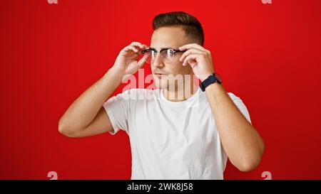 Hübscher junger hispanischer Mann, der die Brille vor einem roten isolierten Hintergrund stellt und Selbstvertrauen darstellt Stockfoto