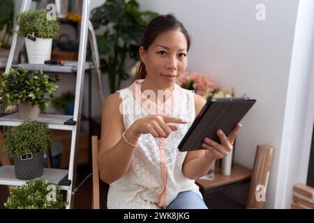 Eine junge asiatische Floristin, die selbstbewusst mit dem Touchpad im Blumenladen lächelt Stockfoto
