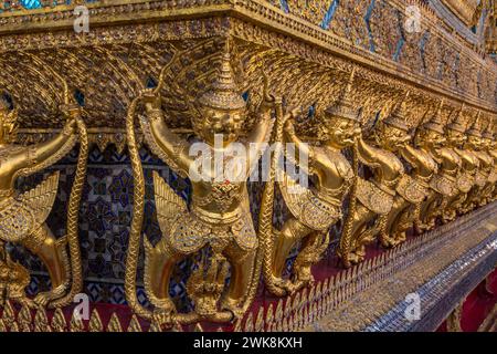 Goldene Statuen von Garuda vs. Naga bewachen den Tempel des Smaragdbuddhas im Grand Palace Complex in Bangkok, Thailand. Stockfoto