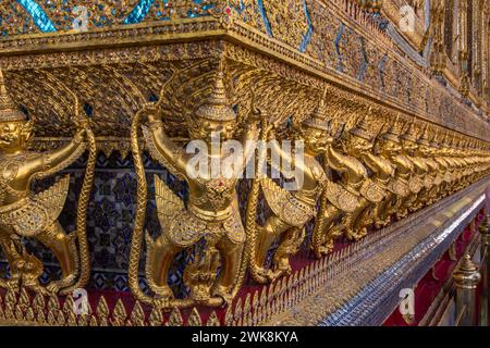 Goldene Statuen von Garuda vs. Naga bewachen den Tempel des Smaragdbuddhas im Grand Palace Complex in Bangkok, Thailand. Stockfoto