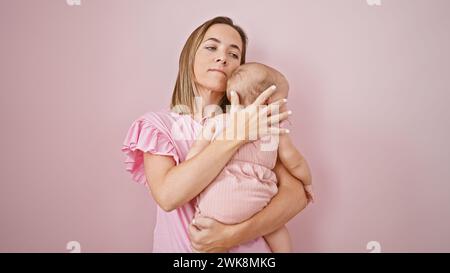 Entspannte Mutter umarmt und hält ihr Baby über einem kühlen, hübschen rosa isolierten Hintergrund und drückt ernsthafte Liebe in ihrem lässigen Lebensstil aus, strengthe Stockfoto