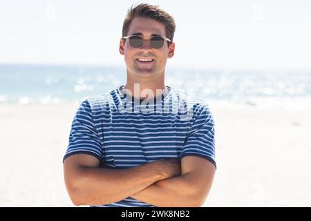 Junger Mann steht selbstbewusst an einem sonnigen Strand Stockfoto
