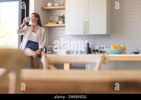Eine junge kaukasische Frau genießt eine Tasse Kaffee in einer modernen Küche mit unverändertem Kopierraum Stockfoto
