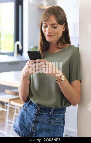 Eine Kaukasierin mittleren Alters ist lässig gekleidet und lächelt, während sie ihr Smartphone benutzt Stockfoto