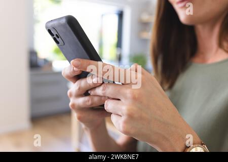 Eine junge kaukasische Frau konzentriert sich darauf, ihr Smartphone zu benutzen Stockfoto
