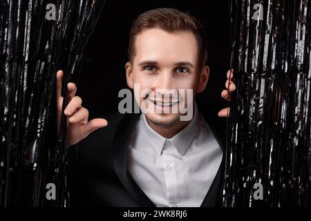 Glücklicher, gutaussehender Mann in schwarzer Jacke, der auf Glitzerhintergrund lächelt. Stockfoto