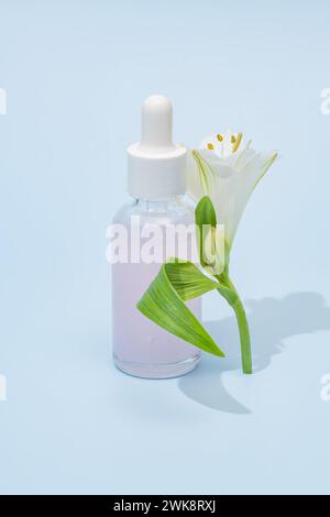 Kosmetikflasche aus rosa Glas mit Tropfer und Alstromeria-Blume auf blauem Hintergrund. Naturkosmetikkonzept, natürliches ätherisches Öl und Hautpflege Stockfoto