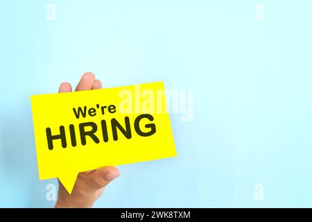 Menschliche Hand hält gelbe Sprechblase mit geschriebenem Satz Wir stellen ein. Recruitment- und Einstellungskonzept. Stockfoto