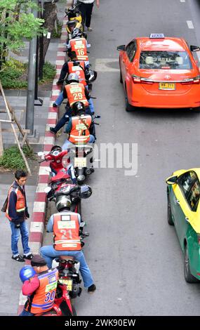 Blick von oben auf eine Reihe von Motorradtaxifahrern, die auf Kunden warten, und Autotaxis, die an ihnen vorbeifahren, auf der Silom Road im Zentrum von Bangkok, Thailand, Asien. Stockfoto