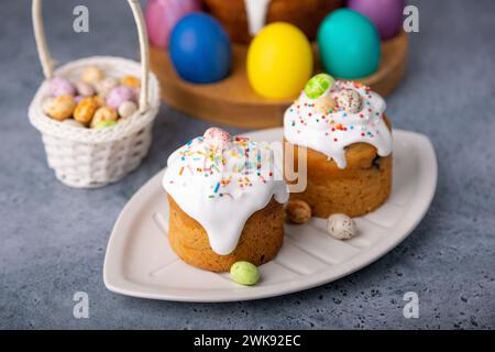 Zwei kleine Osterkulichs mit kandierten Früchten in weißer Glasur mit bunten Streuseln im Schnitt. Bemaltes Hühnchen und Wachteleier. Traditionelle Osterbak Stockfoto