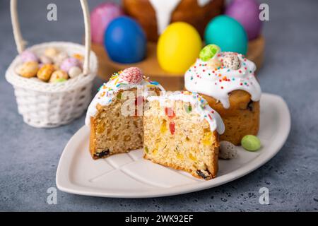 Zwei kleine Osterkulichs mit kandierten Früchten in weißer Glasur mit bunten Streuseln im Schnitt. Bemaltes Hühnchen und Wachteleier. Traditionelle Osterbak Stockfoto