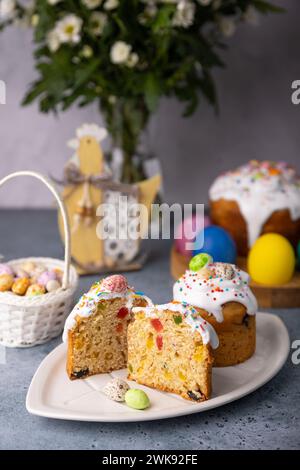 Zwei kleine Osterkulichs mit kandierten Früchten in weißer Glasur mit bunten Streuseln im Schnitt. Bemaltes Hühnchen und Wachteleier. Traditionelle Osterbak Stockfoto