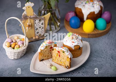 Zwei kleine Osterkulichs mit kandierten Früchten in weißer Glasur mit bunten Streuseln im Schnitt. Bemaltes Hühnchen und Wachteleier. Traditionelle Osterbak Stockfoto