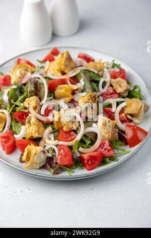 Warmer Salat mit rapan (Schnecken), Tomaten, Zwiebeln, Blattgemüse und Olivenöl. Traditioneller Salat mit Meeresfrüchten. Nahaufnahme, selektiver Fokus. Stockfoto