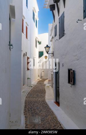 Binibeca Vell, Spanien - 24. Januar 2024: Enge Gasse führt durch ein Labyrinth von weiß getünchten Gebäuden im Dorfzentrum von Binibeca Vell Stockfoto