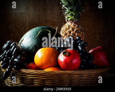 Die verschiedenen Früchte in einem Korb auf einem alten Holztisch vor walnussbraunem Hintergrund. Stockfoto