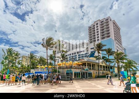 Hollywood Beach, FL - USA - 9. Februar 2024 Dreiviertelansicht von Touristen, die auf der Promenade spazieren gehen, vorbei am berühmten Margaritaville Beach Resort, einem Leuchtturm Stockfoto