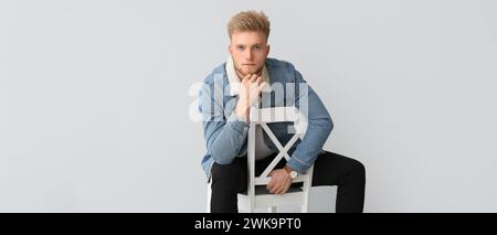 Porträt eines gutaussehenden jungen Mannes, der auf einem Stuhl vor hellem Hintergrund sitzt Stockfoto