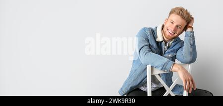 Porträt eines gutaussehenden, lächelnden jungen Mannes, der auf Stuhl vor hellem Hintergrund sitzt und Platz für Text hat Stockfoto