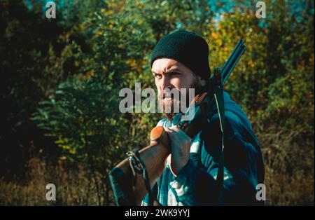 Bärtiger Jäger mit Waffe und Spaziergang im Wald. Jäger mit Schrotflinte auf der Jagd. Stockfoto