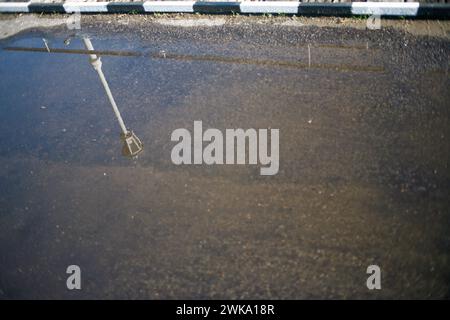 Die Reflexion eines altmodischen Straßenlaternenpfosten in einer Regenpfütze auf einer alten Brücke Stockfoto