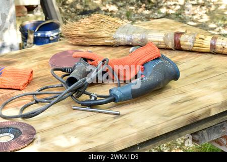 Ein Bohrer, Handschuhe und eine Schleifscheibe, ein Schreinerwerkzeug liegen auf einer Werkbank. Stockfoto