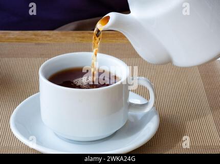 Ein frischer Tee, der aus einer traditionellen englischen Teekanne in eine porzellantasse auf einer Untertasse gegossen wird. Es ist ein kräftiges Bier ohne Milch Stockfoto