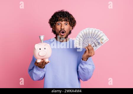 Foto von verrücktem, fröhlichem Kerl mit offenem Mund tragen trendige Kleidung, die Schweinebank zeigt, Gehaltsspeicher isoliert auf rosa Hintergrund zu retten Stockfoto