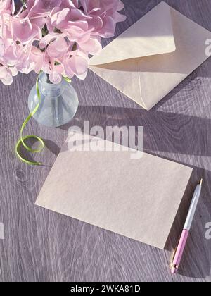 Vase mit rosa Blumen neben einem Stück Papier. Kopierraum auf leerer Grußkarte. Stockfoto