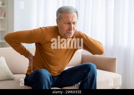 Ein verärgerter älterer Mann fühlt plötzliche Rückenschmerzen Stockfoto