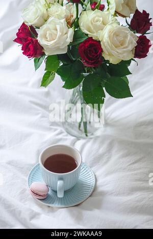 Eine Vase mit roten und weißen Rosen neben einer Tasse Kaffee Stockfoto